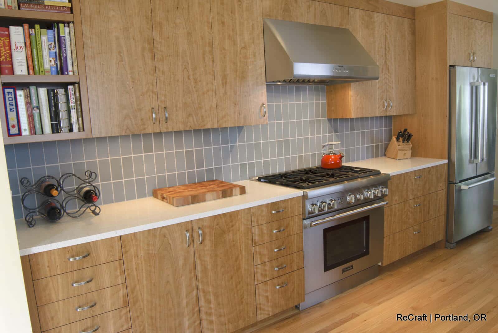Modern kitchen with wooden cabinets, stainless steel appliances, tiled backsplash, and a countertop featuring a chopping board and a knife block. A wine rack with bottles is placed on the counter. Modern kitchen with wooden cabinets, stainless steel appliances, tiled backsplash, and a countertop featuring a chopping board and a knife block. A wine rack with bottles is placed on the counter.