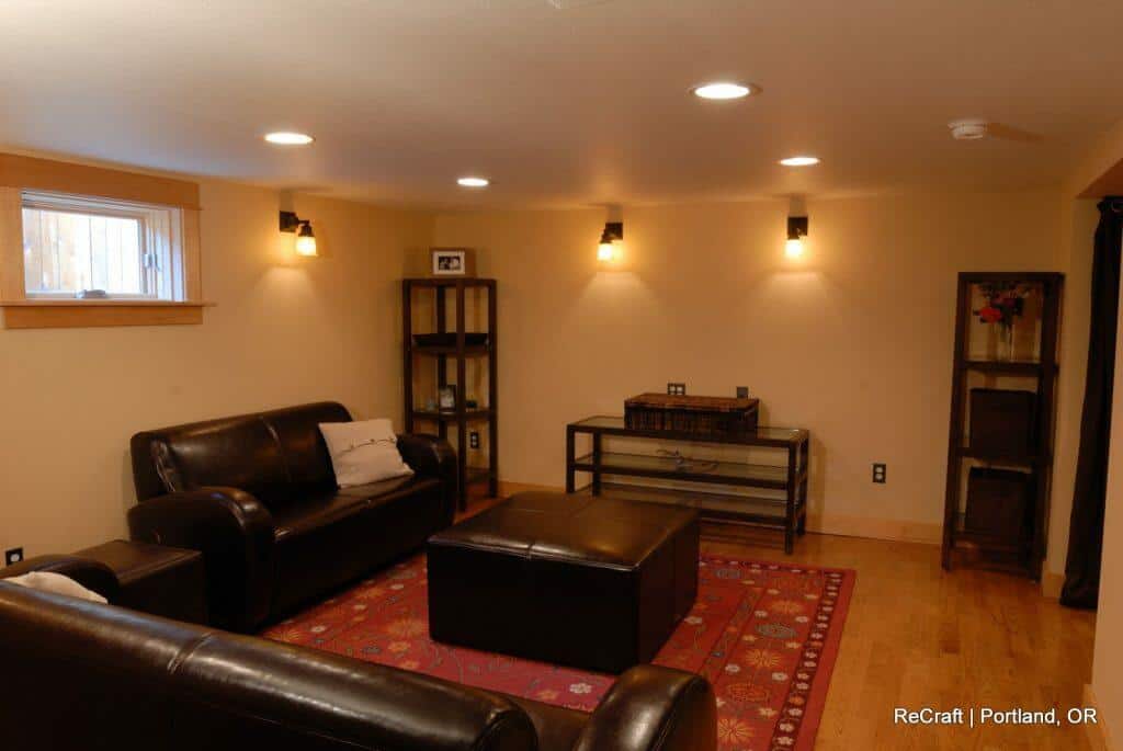 A cozy living room with brown leather furniture, a red patterned rug, and wall-mounted lighting. There are shelves with decor items against tan walls. A cozy living room with brown leather furniture, a red patterned rug, and wall-mounted lighting. There are shelves with decor items against tan walls.