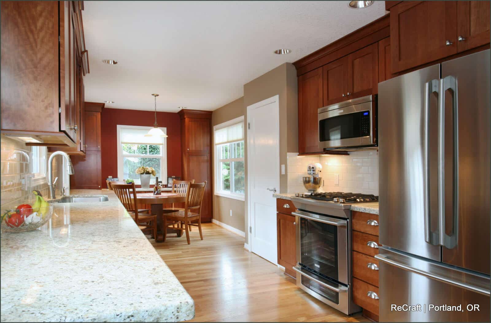 A modern kitchen with stainless steel appliances, wooden cabinets, granite countertops, and a dining area with a table and chairs near a window. A modern kitchen with stainless steel appliances, wooden cabinets, granite countertops, and a dining area with a table and chairs near a window.