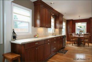 A kitchen with wooden cabinets, granite countertops, and a hardwood floor. A sink, dishwasher, and dining table with four chairs are visible. A window provides natural light. Text reads 