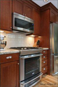 A modern kitchen with dark wood cabinets, stainless steel appliances including a microwave and oven, a granite countertop, and a white subway tile backsplash.