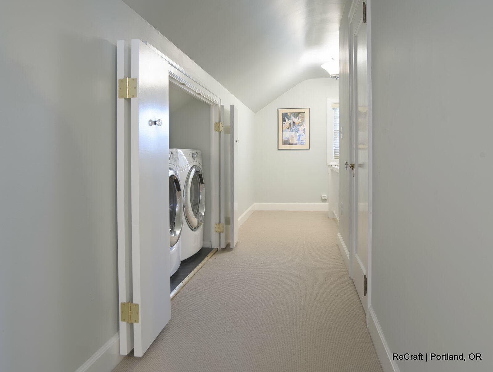 Hallway featuring a laundry area with modern washing machines, light gray walls, and framed artwork, showcasing ReCraft Home Remodeling's interior design and home remodeling capabilities in Portland.