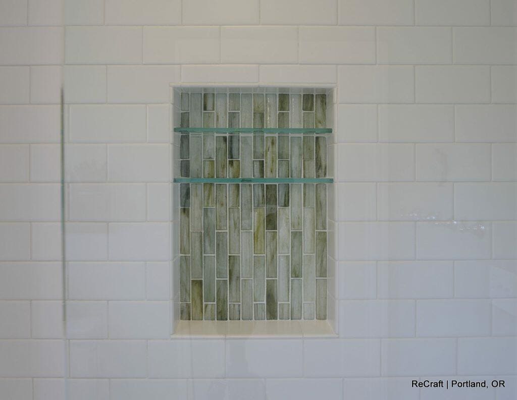 Close-up of a shower wall featuring white subway tiles and a recessed niche with greenish glass and stone mosaic tiles. Close-up of a shower wall featuring white subway tiles and a recessed niche with greenish glass and stone mosaic tiles.