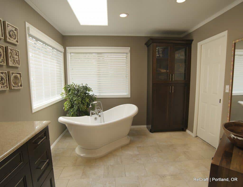 A spacious bathroom with a freestanding white bathtub, a dark wooden cabinet, a potted plant, wall art, and a skylight. The floor is tiled, and the room has both natural and artificial light. A spacious bathroom with a freestanding white bathtub, a dark wooden cabinet, a potted plant, wall art, and a skylight. The floor is tiled, and the room has both natural and artificial light.