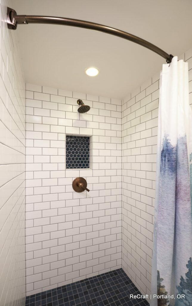 White-tiled shower with a rainfall showerhead, bronze fixtures, a niche with blue hexagonal tiles, and a white and blue shower curtain. White-tiled shower with a rainfall showerhead, bronze fixtures, a niche with blue hexagonal tiles, and a white and blue shower curtain.