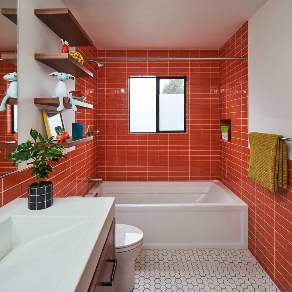 Modern bathroom with orange tiles, a white bathtub, hexagonal white floor tiles, a sink, a black vase with green plant, shelves with decor items, and a window above the bathtub. Modern bathroom with orange tiles, a white bathtub, hexagonal white floor tiles, a sink, a black vase with green plant, shelves with decor items, and a window above the bathtub.