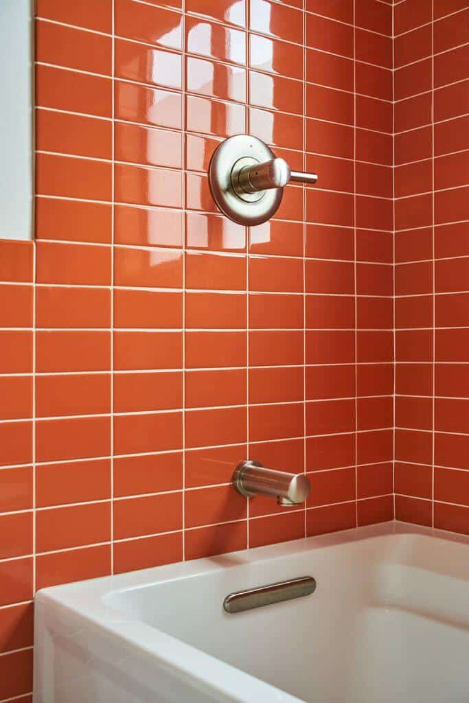 A white bathtub with a chrome faucet and shower handle is set against a background of red tiled walls. A white bathtub with a chrome faucet and shower handle is set against a background of red tiled walls.