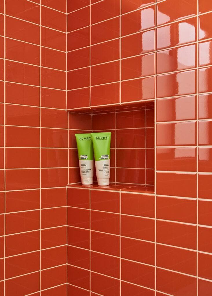 Two green cosmetic tubes on a built-in shelf in a shower with red-orange tiles. Two green cosmetic tubes on a built-in shelf in a shower with red-orange tiles.