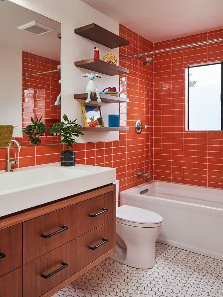 A modern bathroom with bright orange tiles, a white bathtub, a wooden vanity with a white countertop, hexagonal floor tiles, and wall shelves holding decor items. A modern bathroom with bright orange tiles, a white bathtub, a wooden vanity with a white countertop, hexagonal floor tiles, and wall shelves holding decor items.