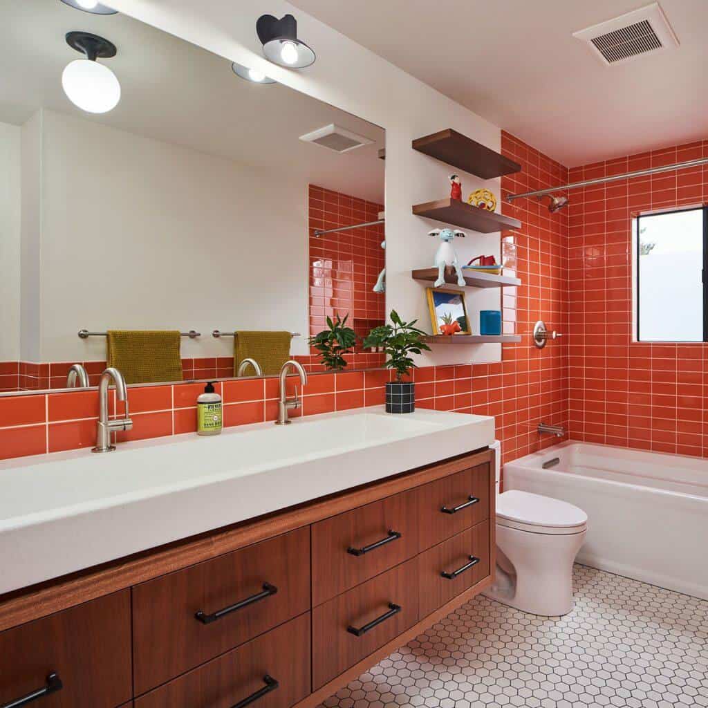 A modern bathroom with red-tiled walls, a white countertop with two sinks, wooden cabinets, a toilet, a bathtub with a shower, and a small window. A modern bathroom with red-tiled walls, a white countertop with two sinks, wooden cabinets, a toilet, a bathtub with a shower, and a small window.