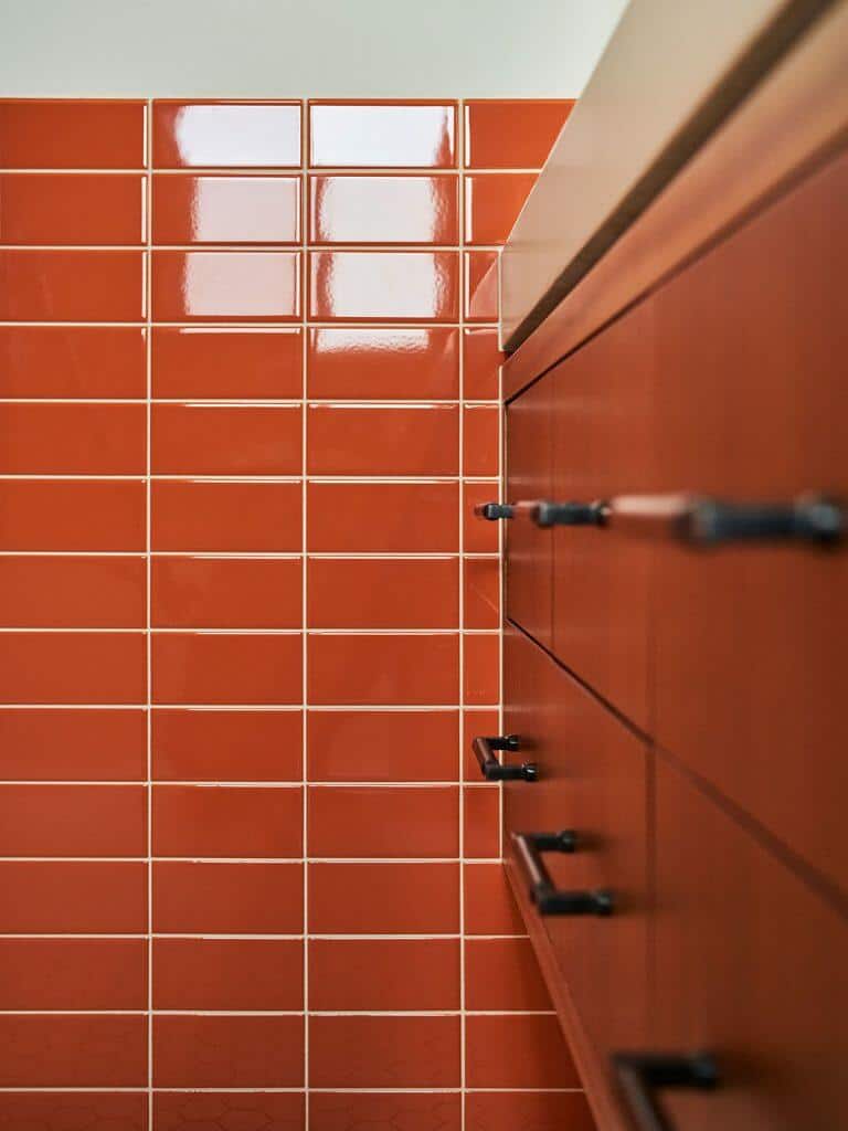 An interior view of a bathroom shows a red-tiled wall adjacent to a wooden cabinet with black handles. An interior view of a bathroom shows a red-tiled wall adjacent to a wooden cabinet with black handles.