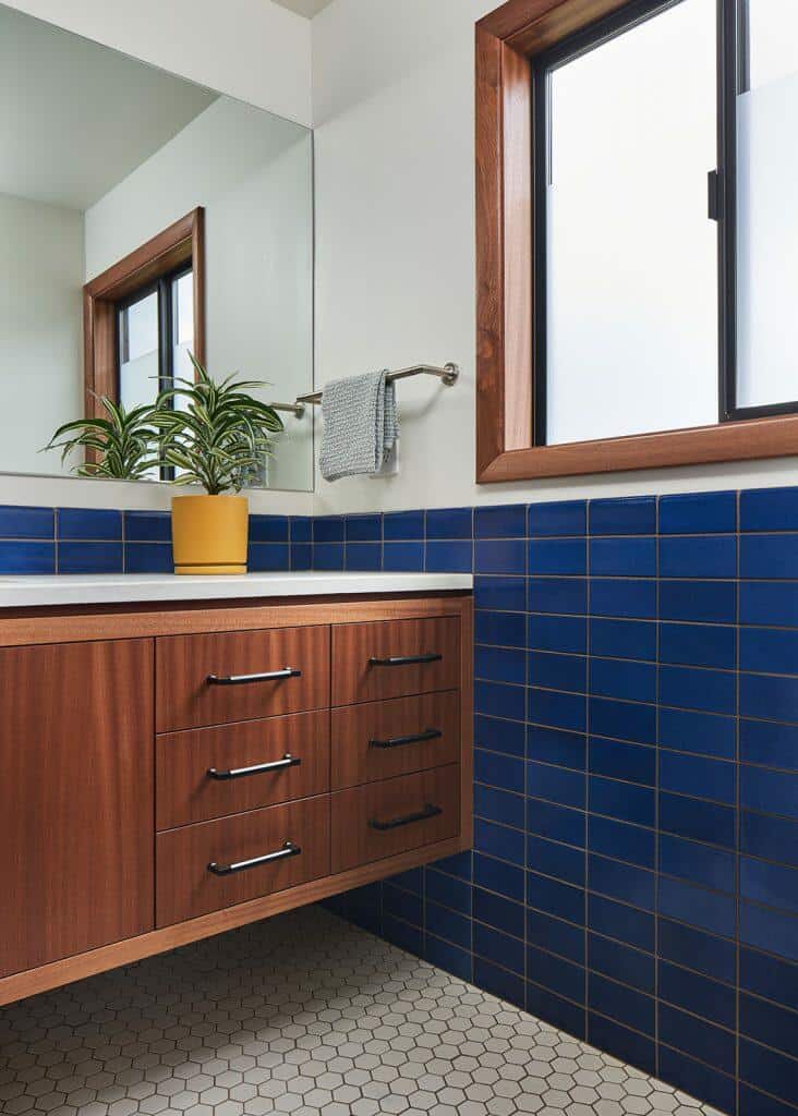 Modern bathroom with a wooden vanity, blue tiled wall, hexagonal floor tiles, a potted plant on the counter, and a window with a wooden frame. Modern bathroom with a wooden vanity, blue tiled wall, hexagonal floor tiles, a potted plant on the counter, and a window with a wooden frame.