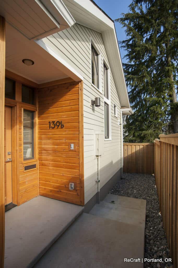 A modern house exterior with a wooden entryway, glass front door, and a vertical house number "139b" on the siding. A gravel path runs alongside a wooden fence. The location is noted as Portland, OR. A modern house exterior with a wooden entryway, glass front door, and a vertical house number "139b" on the siding. A gravel path runs alongside a wooden fence. The location is noted as Portland, OR.