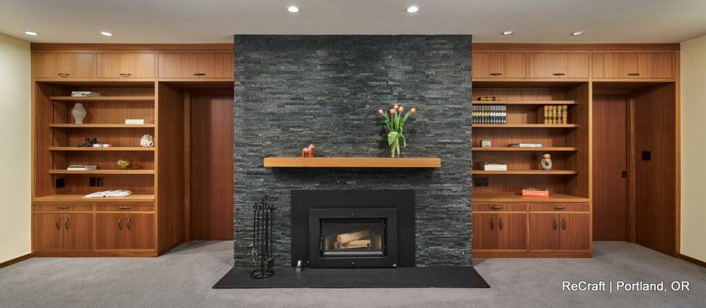 A modern living room features a central fireplace with a stone wall surround, flanked by two wooden built-in shelving units. A mantle holds a vase with orange tulips. A modern living room features a central fireplace with a stone wall surround, flanked by two wooden built-in shelving units. A mantle holds a vase with orange tulips.