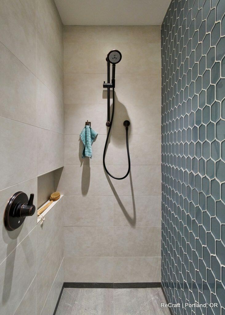 A modern shower with a black handheld showerhead, a blue towel hanging, and a hexagonal tile design on one wall. A modern shower with a black handheld showerhead, a blue towel hanging, and a hexagonal tile design on one wall.