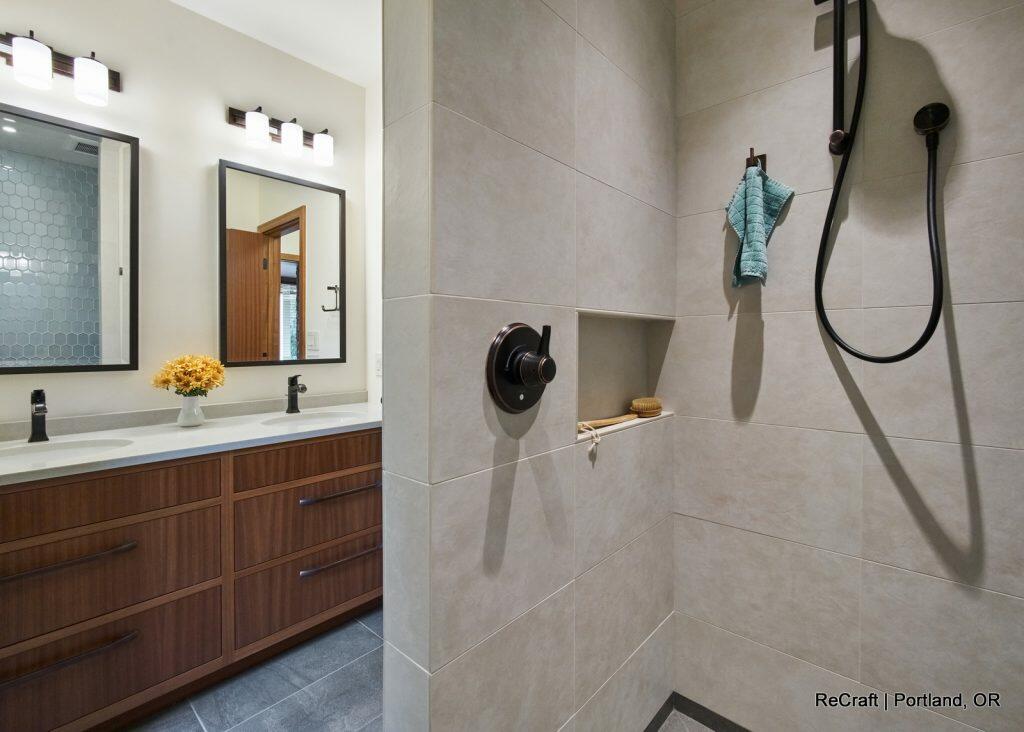 Modern bathroom with double vanity, large mirrors, overhead lighting, and a spacious shower area featuring a built-in shelf, a showerhead, and a towel hanging on the shower handle. Modern bathroom with double vanity, large mirrors, overhead lighting, and a spacious shower area featuring a built-in shelf, a showerhead, and a towel hanging on the shower handle.