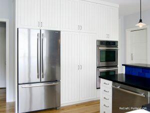 A modern kitchen featuring stainless steel appliances, white cabinetry, and a black countertop island with a blue tile backsplash under a hanging light fixture.