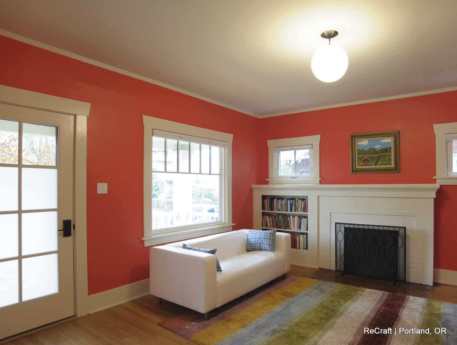 Brightly colored living room with coral walls, white couch, and a cozy fireplace, showcasing ReCraft Home Remodeling's interior design style and remodeling capabilities.