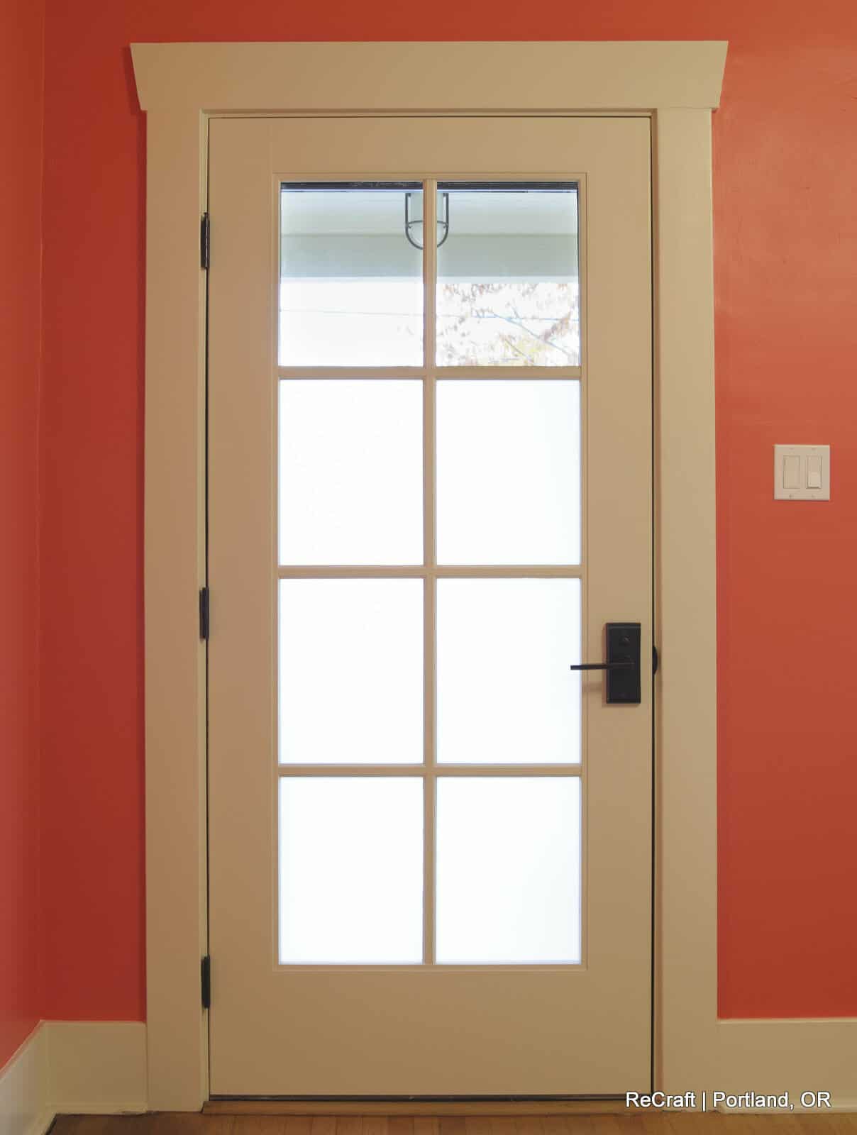 Interior door with glass panes, framed in white, against a coral wall, showcasing ReCraft Home Remodeling's design style for Portland home renovations.