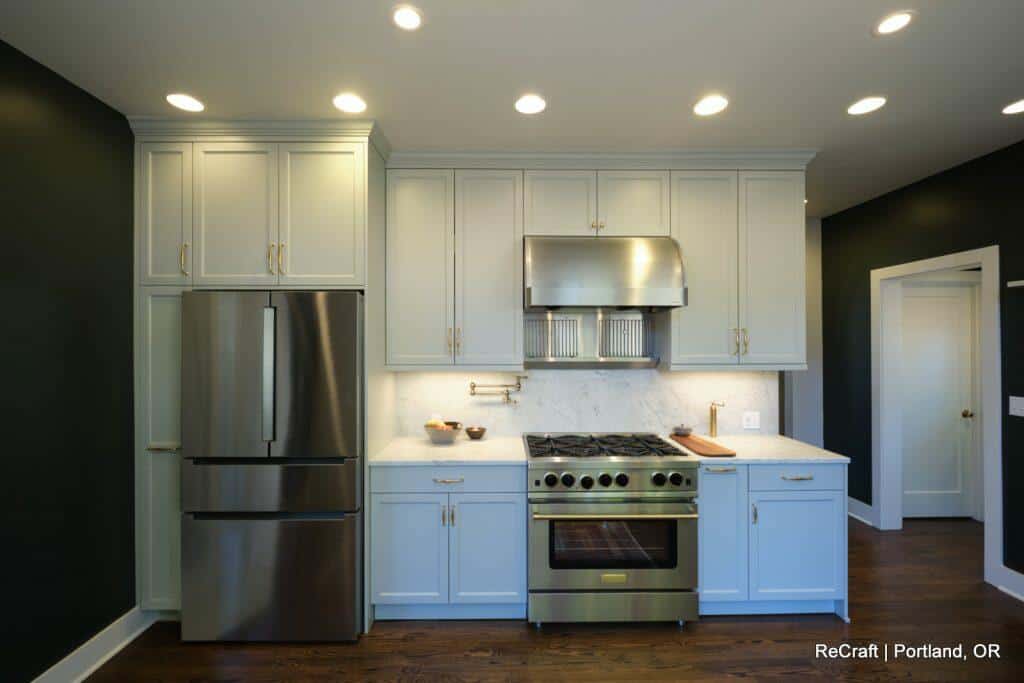 Modern kitchen with dark green walls, stainless steel appliances, white cabinets, marble backsplash, and wood flooring. ReCraft | Portland, OR marked in the bottom right corner. Modern kitchen with dark green walls, stainless steel appliances, white cabinets, marble backsplash, and wood flooring. ReCraft | Portland, OR marked in the bottom right corner.