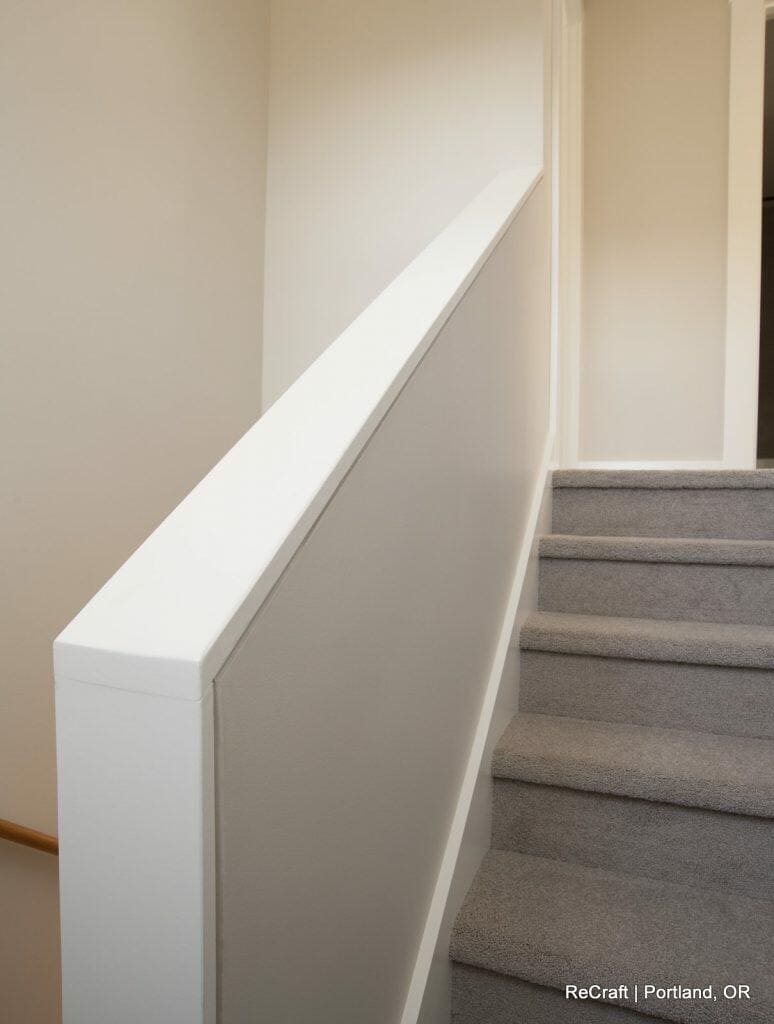 A staircase with grey carpeted steps and a white wall on the left side is shown. The top of the stairs leads to another level. A staircase with grey carpeted steps and a white wall on the left side is shown. The top of the stairs leads to another level.