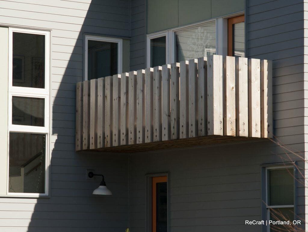 A modern building with gray siding features a small, wooden balcony and several windows. A light fixture is mounted on the wall below the balcony. Text reads "ReCraft | Portland, OR" in the bottom right corner. A modern building with gray siding features a small, wooden balcony and several windows. A light fixture is mounted on the wall below the balcony. Text reads "ReCraft | Portland, OR" in the bottom right corner.