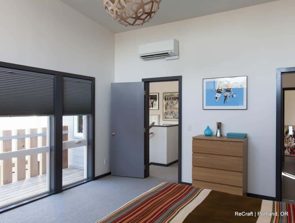 A brightly lit modern bedroom with a large window, wooden dresser, wall art, and a doorway leading to a hallway. A brightly lit modern bedroom with a large window, wooden dresser, wall art, and a doorway leading to a hallway.