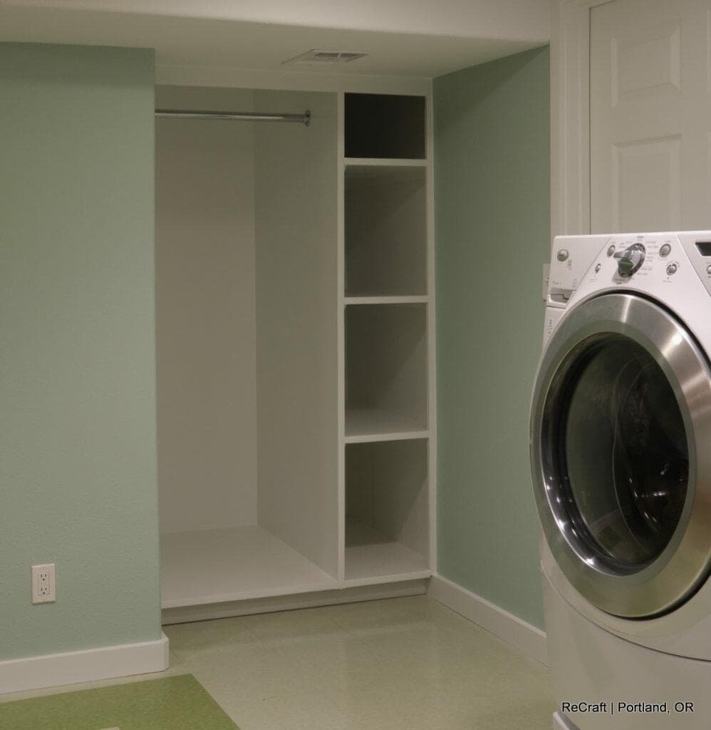 Laundry room with a front-loading washing machine, built-in shelving, and a small open closet. Light green walls and white trim are visible. Laundry room with a front-loading washing machine, built-in shelving, and a small open closet. Light green walls and white trim are visible.