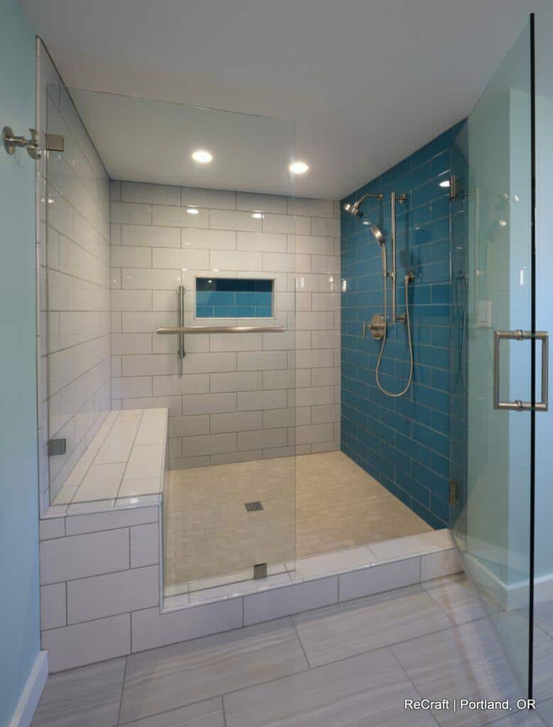 Modern shower with glass enclosure, featuring white and blue subway tiles, a built-in bench, handheld and overhead shower heads, and a recessed shelf. Modern shower with glass enclosure, featuring white and blue subway tiles, a built-in bench, handheld and overhead shower heads, and a recessed shelf.