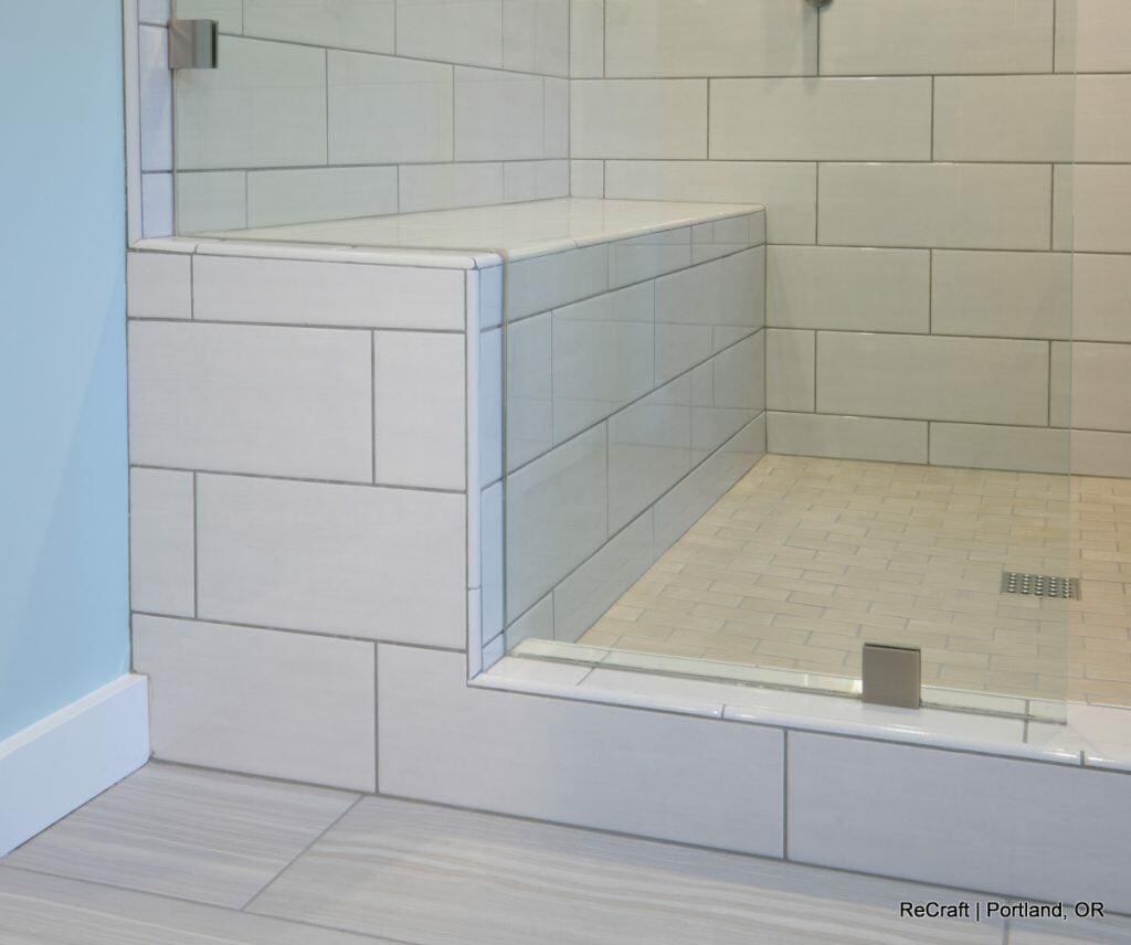 A tiled shower with a built-in bench and glass door, featuring large beige tiles on the walls and smaller beige tiles on the floor. A tiled shower with a built-in bench and glass door, featuring large beige tiles on the walls and smaller beige tiles on the floor.