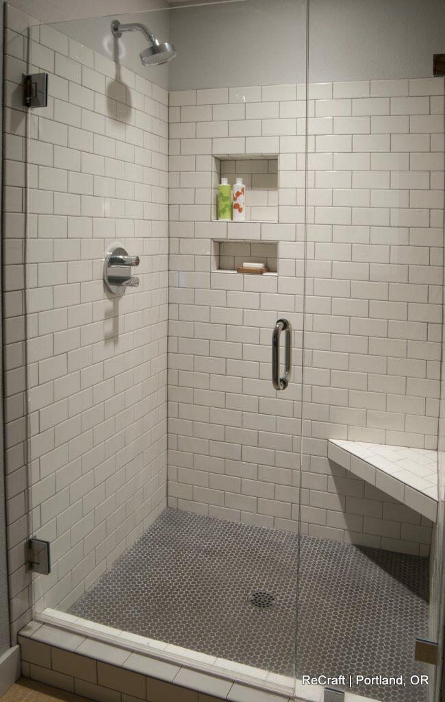 A modern shower with white subway tiles, a glass door, two recessed shelves with toiletries, a chrome showerhead, and a built-in bench. A modern shower with white subway tiles, a glass door, two recessed shelves with toiletries, a chrome showerhead, and a built-in bench.