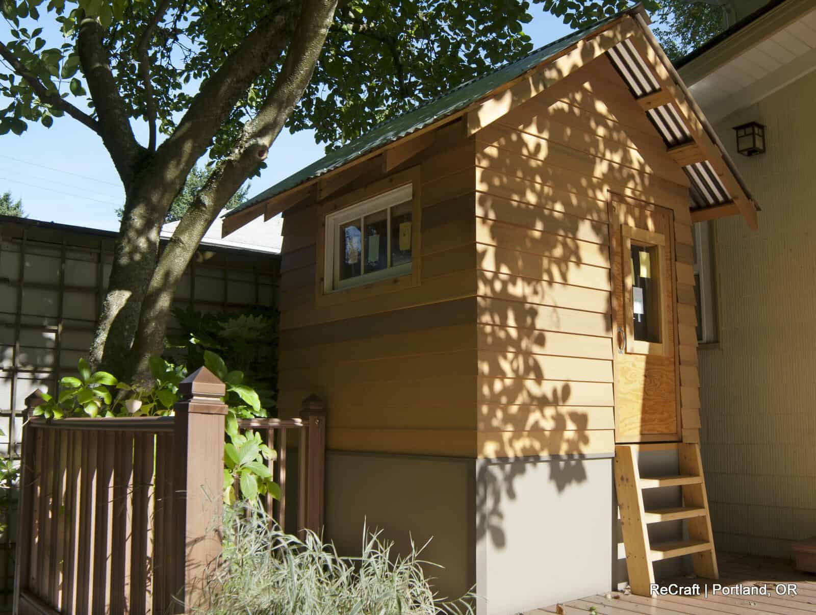 Treehouse with wooden exterior, steps leading to the entrance, surrounded by greenery, showcasing ReCraft Home Remodeling's creative outdoor remodeling project in Portland.