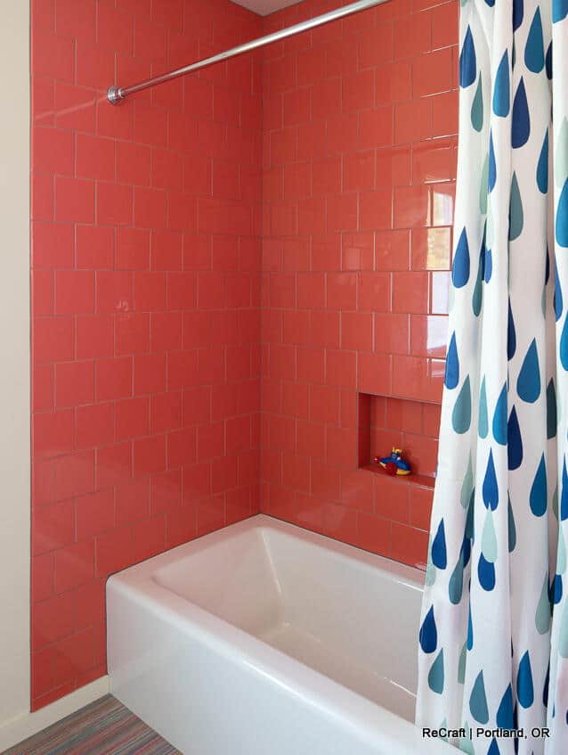 A bathroom with coral-colored tiled walls, a white bathtub, and a shower curtain with blue raindrop patterns. There is a small niche in the wall holding a toy duck. A bathroom with coral-colored tiled walls, a white bathtub, and a shower curtain with blue raindrop patterns. There is a small niche in the wall holding a toy duck.