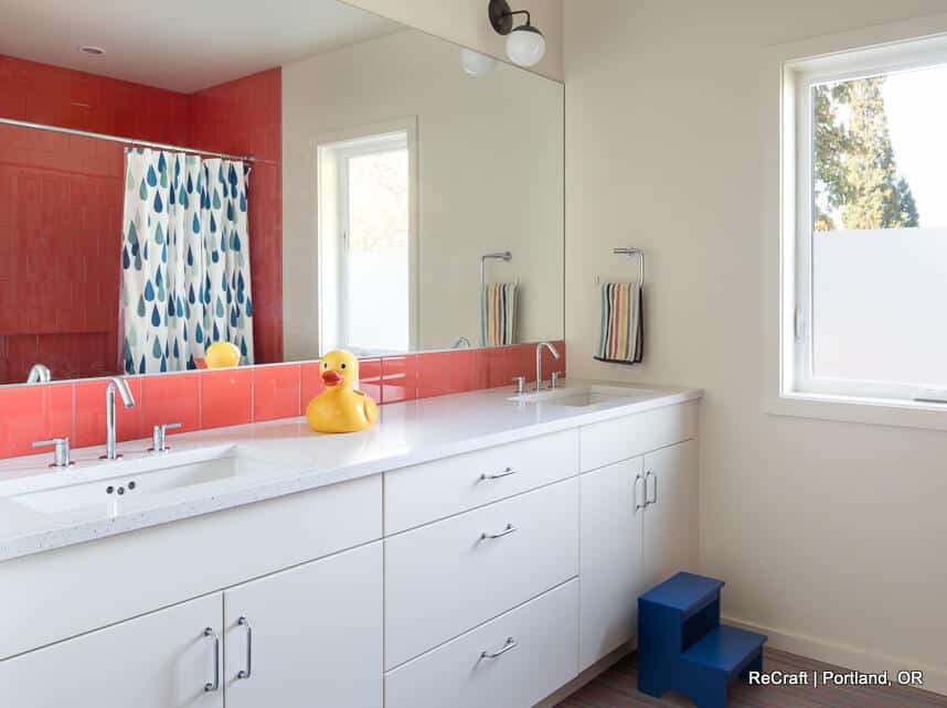 Modern bathroom with a double sink vanity, large mirror, red-tiled backsplash, rubber duck, small stool, and a shower with a patterned curtain. Natural light enters through a window. Modern bathroom with a double sink vanity, large mirror, red-tiled backsplash, rubber duck, small stool, and a shower with a patterned curtain. Natural light enters through a window.