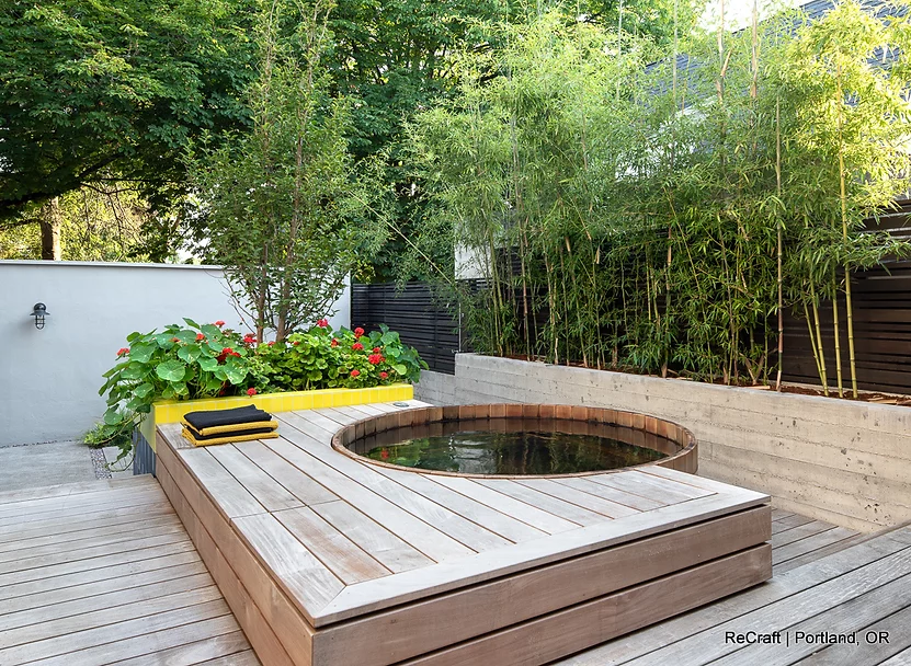 Modern outdoor garden space featuring a circular wooden hot tub, surrounded by lush greenery and vibrant flowers, showcasing ReCraft Home Remodeling's creative landscaping and remodeling expertise.