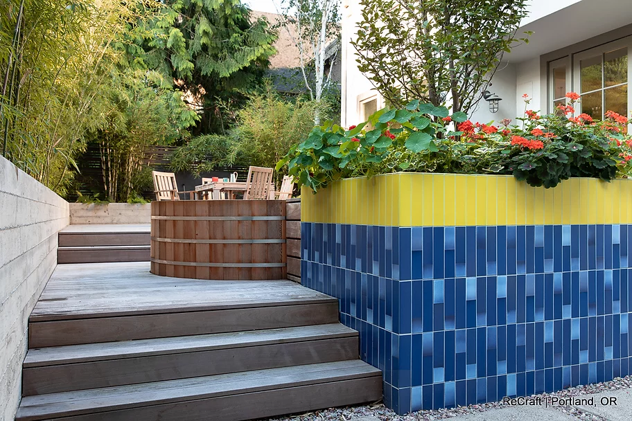 Modern outdoor garden featuring stylish wooden steps leading to a raised planter with vibrant flowers and blue tile accents, showcasing ReCraft Home Remodeling's creative landscaping design.