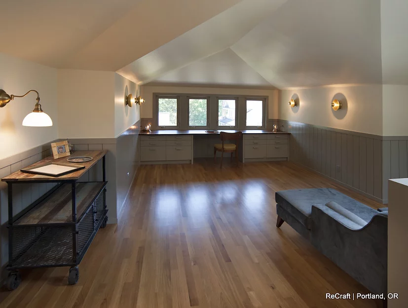 Modern office space with hardwood flooring, large windows, a gray couch, and stylish wall sconces, showcasing ReCraft Home Remodeling's design capabilities in Portland.