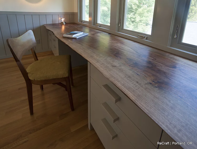 Home office space featuring a wooden desk with a smooth finish, a chair with a yellow cushion, and large windows providing natural light, showcasing ReCraft Home Remodeling's design capabilities in Portland.