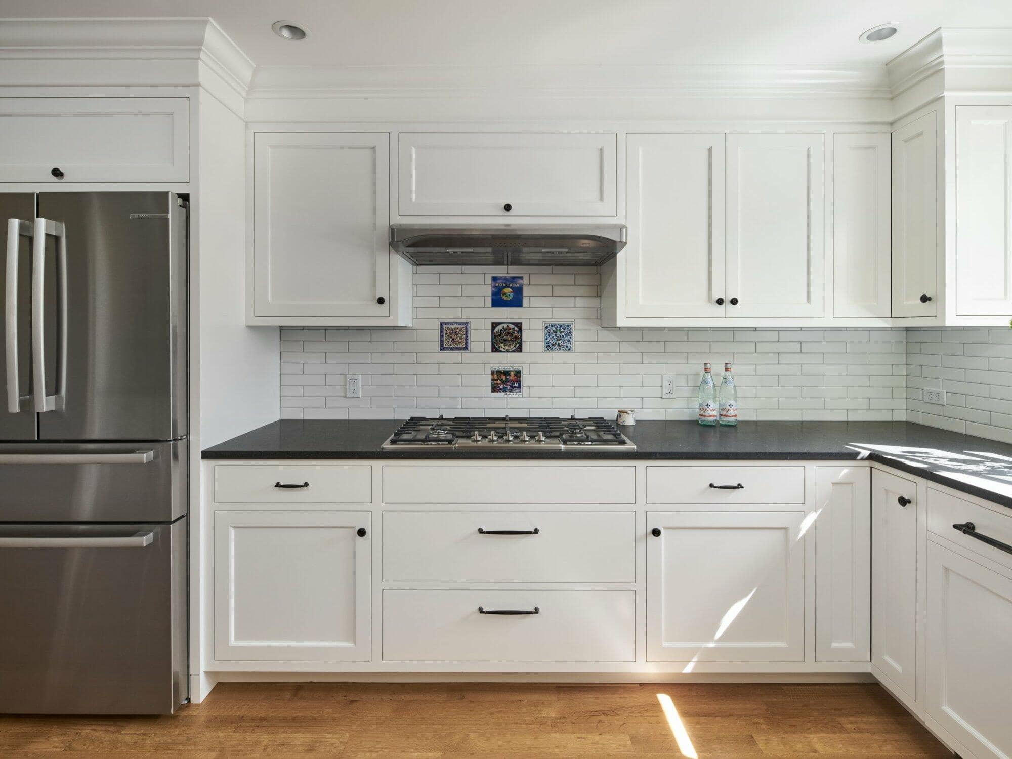 A modern kitchen with white cabinets, black countertops, stainless steel appliances, a gas stove, and decorative tiles above the stove, illuminated by natural light. A modern kitchen with white cabinets, black countertops, stainless steel appliances, a gas stove, and decorative tiles above the stove, illuminated by natural light.