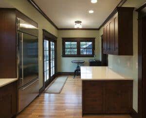 A modern kitchen featuring wooden cabinets, a stainless steel refrigerator, a small table and chairs by the windows, and a door leading outside.