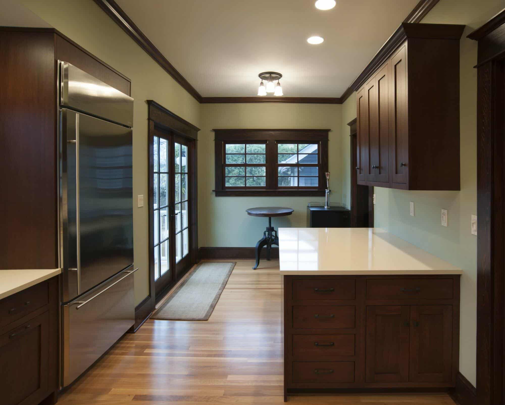 A modern kitchen featuring wooden cabinets, a stainless steel refrigerator, a small table and chairs by the windows, and a door leading outside. A modern kitchen featuring wooden cabinets, a stainless steel refrigerator, a small table and chairs by the windows, and a door leading outside.