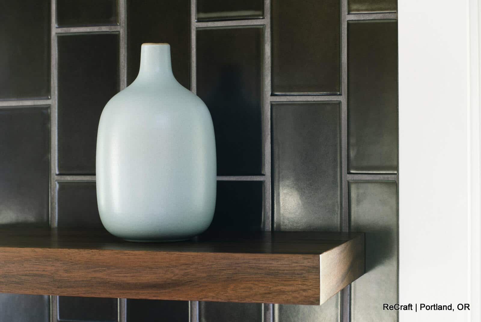 A light blue vase sits on a wooden shelf against a dark tiled wall. Text in the bottom right corner reads A light blue vase sits on a wooden shelf against a dark tiled wall. Text in the bottom right corner reads