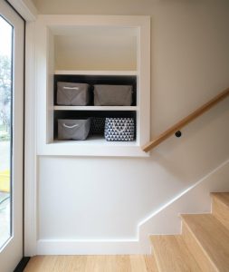 Built-in wall shelves with three storage bins, located beside a wooden staircase and a glass door.
