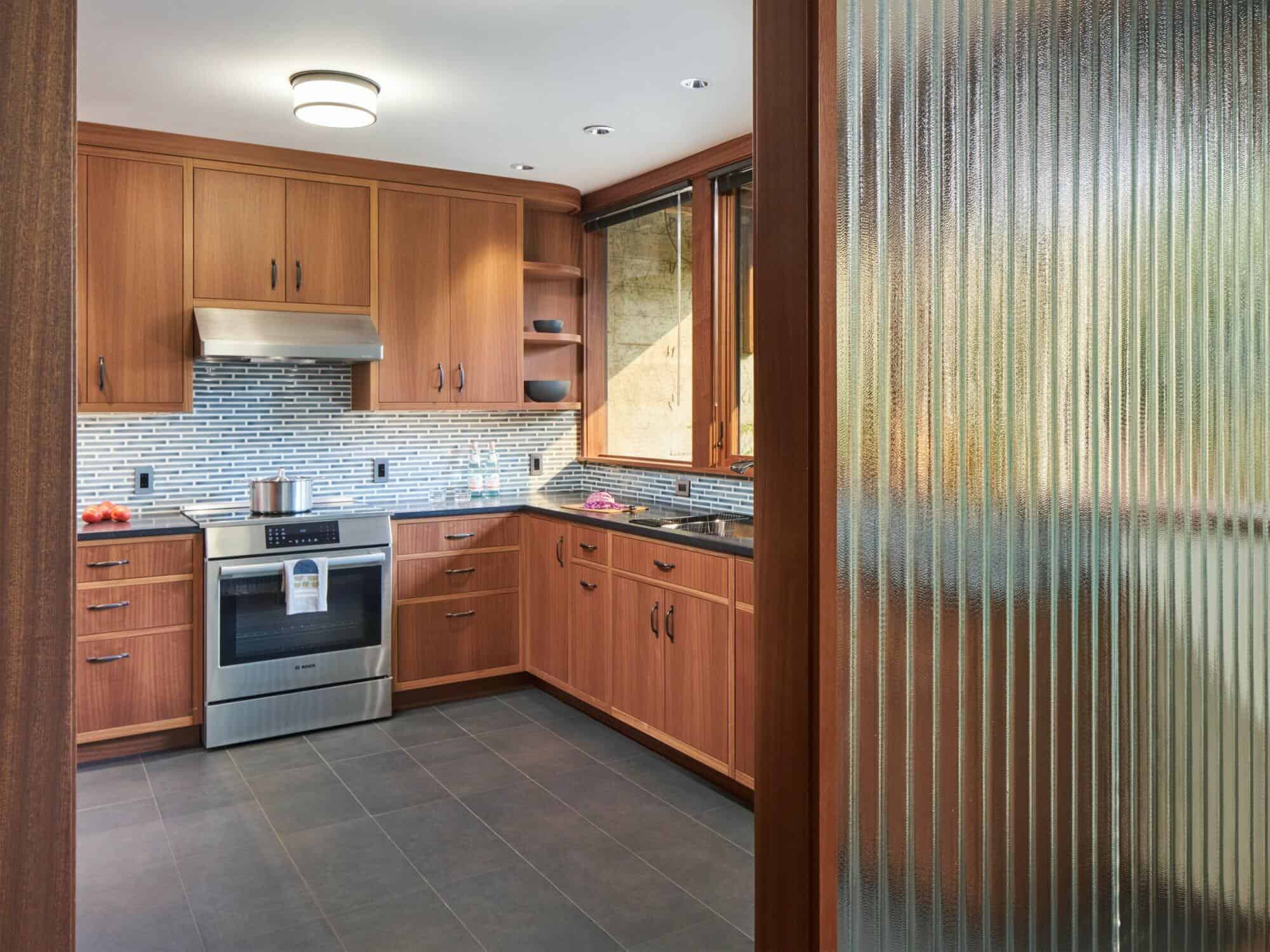A modern kitchen with wooden cabinets, stainless steel appliances, a tile backsplash, and a frosted glass door partially open. A modern kitchen with wooden cabinets, stainless steel appliances, a tile backsplash, and a frosted glass door partially open.