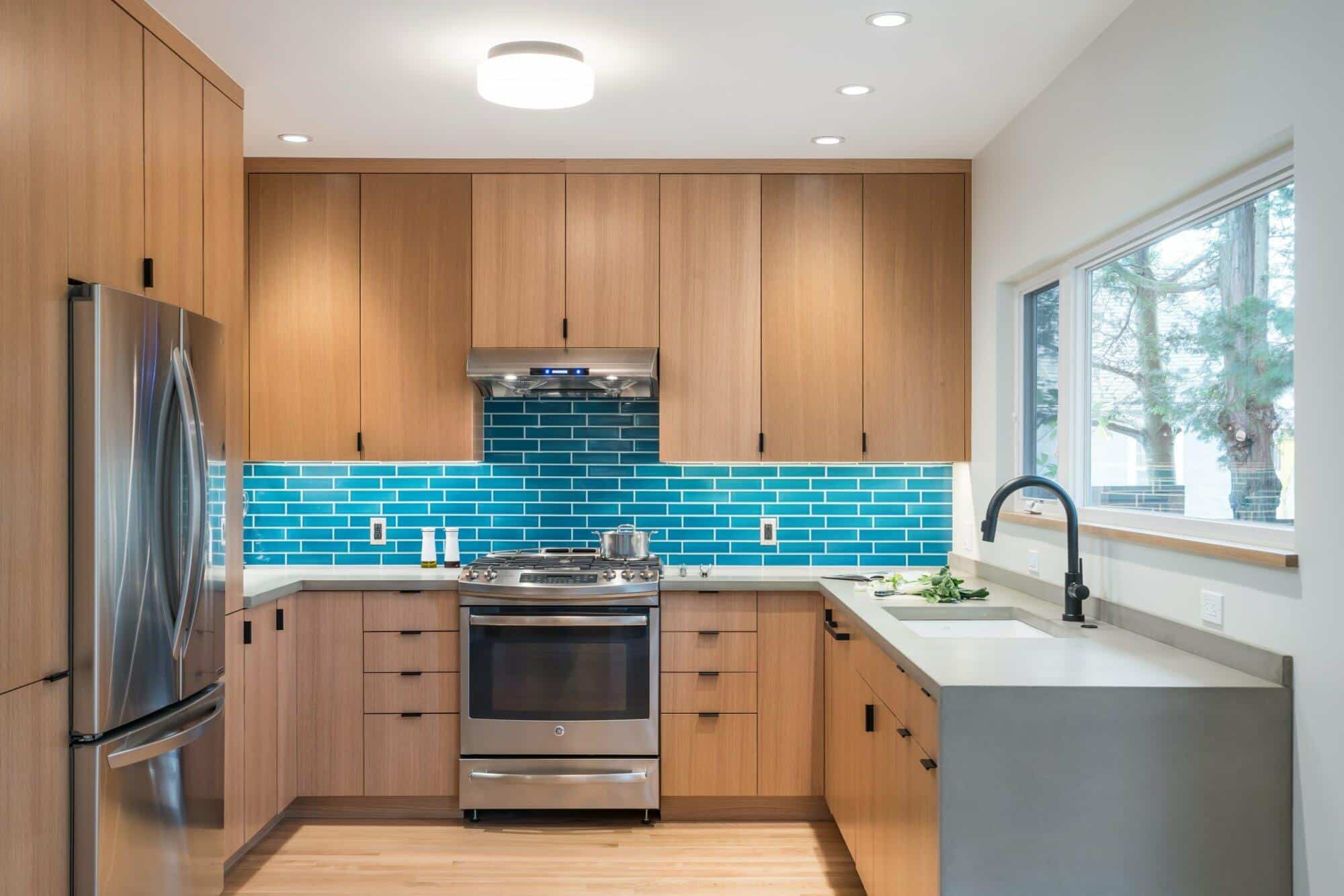 Modern kitchen with wooden cabinets, stainless steel appliances, blue tile backsplash, and a large window over the sink. Modern kitchen with wooden cabinets, stainless steel appliances, blue tile backsplash, and a large window over the sink.