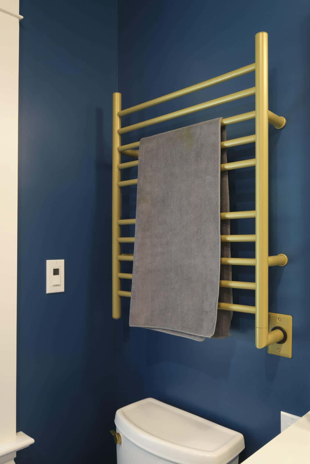 A gold towel rack with a gray towel hanging on it is mounted on a blue wall above a white toilet in a bathroom.