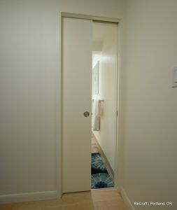 A partially open sliding door reveals a glimpse of a bathroom with a blue floral rug and white towels hanging on a rail.