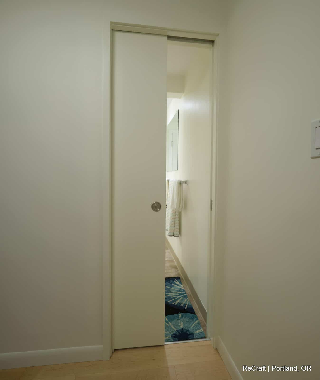 Pocket door leading to a remodeled bathroom, showcasing modern design elements and a clean aesthetic in a Portland basement renovation.