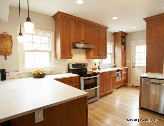 A modern kitchen with wooden cabinets, stainless steel appliances, white countertops, and a white subway tile backsplash. The room has hardwood floors and a back door with a window. A modern kitchen with wooden cabinets, stainless steel appliances, white countertops, and a white subway tile backsplash. The room has hardwood floors and a back door with a window.