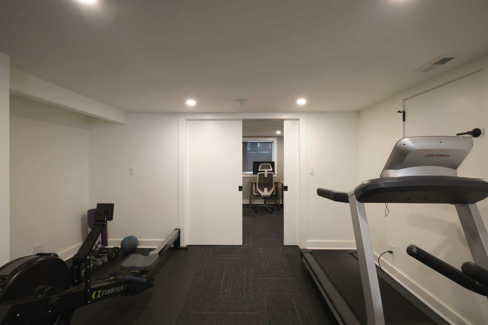 Workout room with treadmill and rowing machine leading to an office space, showcasing basement remodeling by ReCraft Home Remodeling Portland.